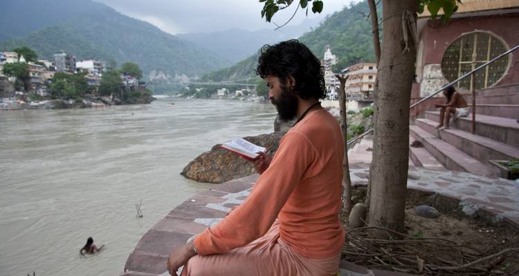 Personne assise au bord d'une rivière en train de lire un livre.