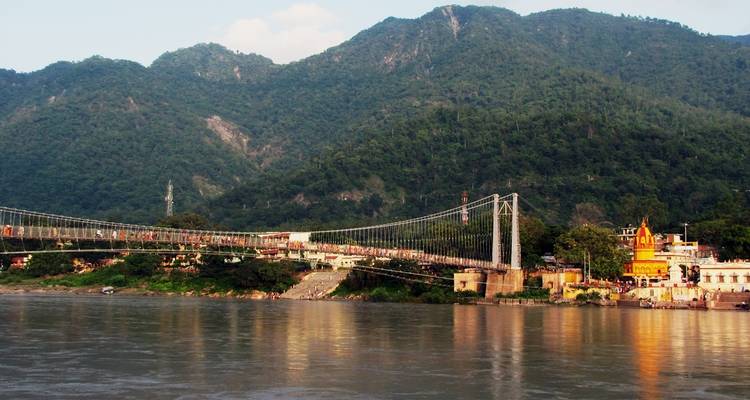 Pont suspendu au-dessus d'une rivière avec un arrière-plan vallonné.