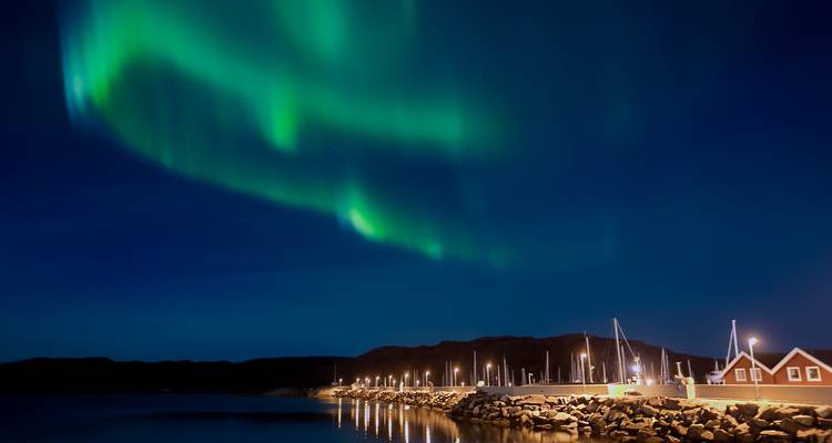 Aurores boréales illuminant un paisible village au bord de l'eau la nuit.