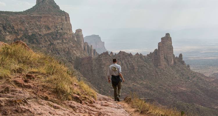 Un senderista trekking por un camino rocoso en el acantilado con vistas a impresionantes agujas de arenisca y un valle enorme.