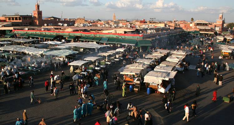 Vista amplia de la plaza Jemaa el-Fnaa llena de puestos de mercado, humo de las parrillas y multitudes de locales y turistas.