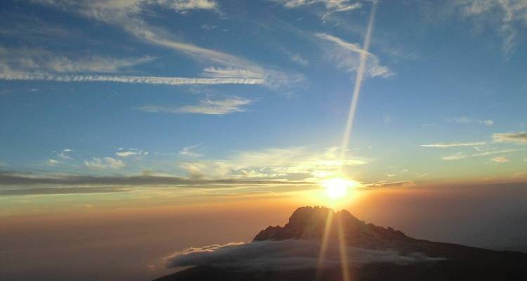 Ein Sonnenaufgangsblick von einem Berggipfel mit Wolken darunter.