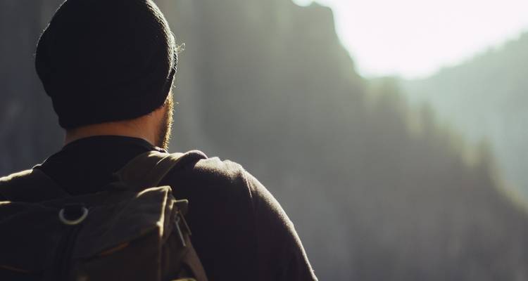 Person mit einem Rucksack, die auf eine bergige Landschaft blickt.