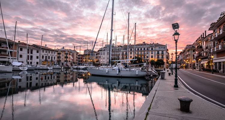 Marina tranquila bordeada de veleros que reflejan los cielos rosados del amanecer en un pueblito costero italiano