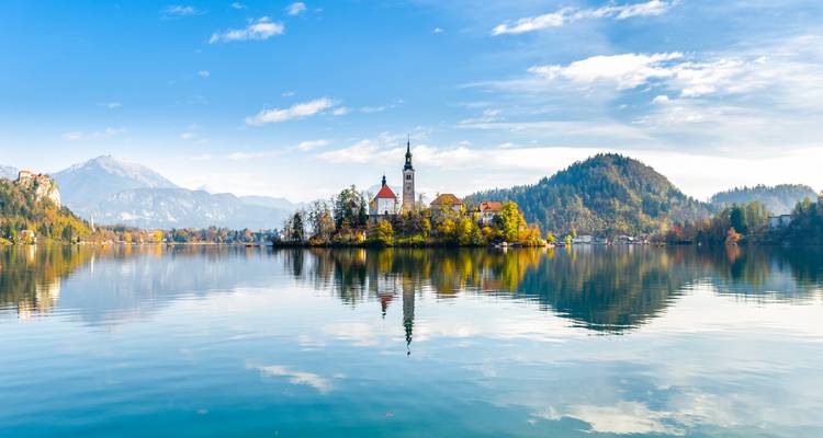 Lago de Bled con aguas tranquilas como un espejo reflejando su iglesia en la isla, las colinas boscosas de alrededor y los Alpes a lo lejos