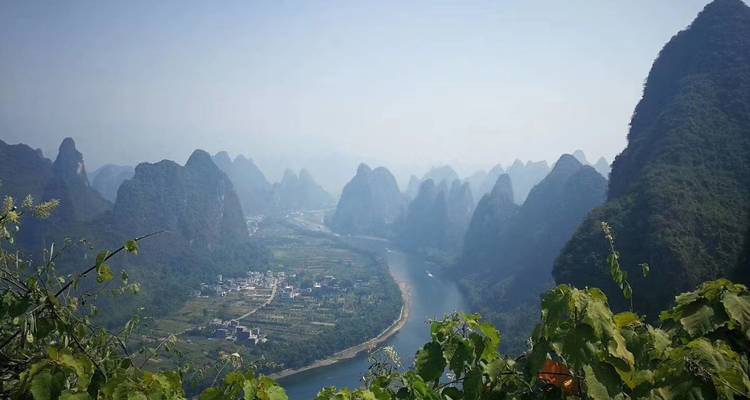 Vista elevada del río Li serpenteando entre picos de karst empinados con un pequeño pueblo rural abajo.