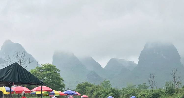 Coloridos paraguas protegen a los visitantes a lo largo de un río cubierto de niebla bajo imponentes montañas de karst.