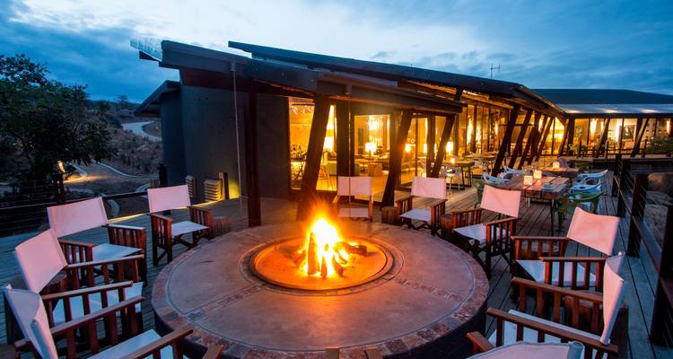 Modern lodge with a circular fire pit and seating at dusk.