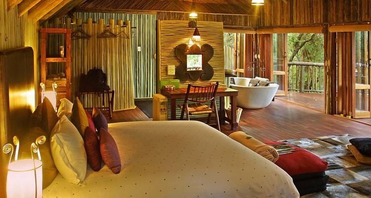 Elegant eco-lodge interior with bed facing open-view deck.
