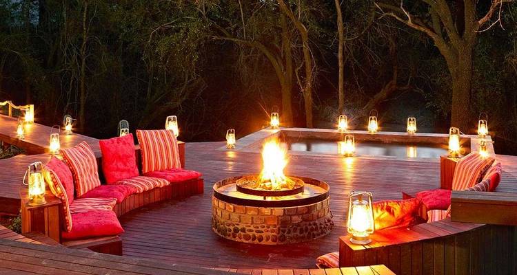 Coin salon extérieur confortable avec foyer et lanternes au crépuscule.