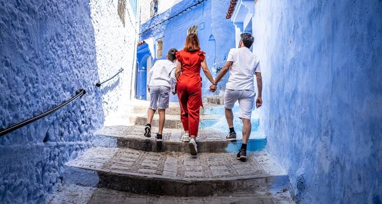 Family ascends a narrow, cobalt-blue lane in Chefchaouen surrounded by vibrantly painted walls.