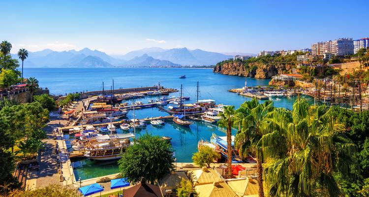 Las aguas turquesas del Mediterráneo bañan el pintoresco puerto de Antalya bordeado de embarcaciones, palmeras y escarpados acantilados costeros.