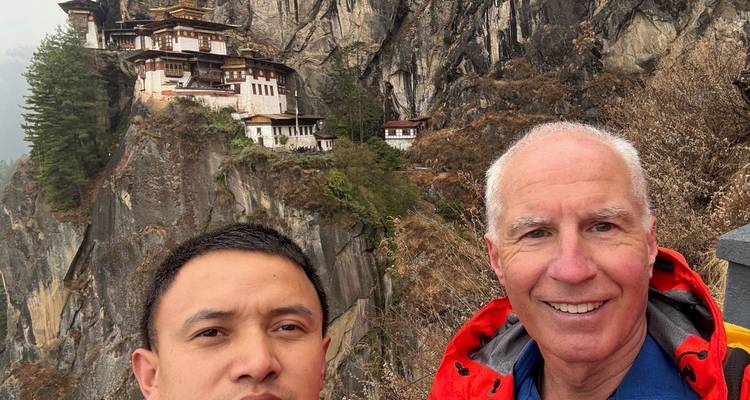 Deux personnes prenant un selfie avec le monastère du Nid du Tigre en arrière-plan.