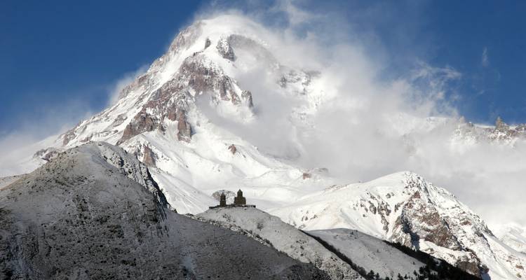 Una cima cubierta de nieve con una pequeña iglesia en su base.