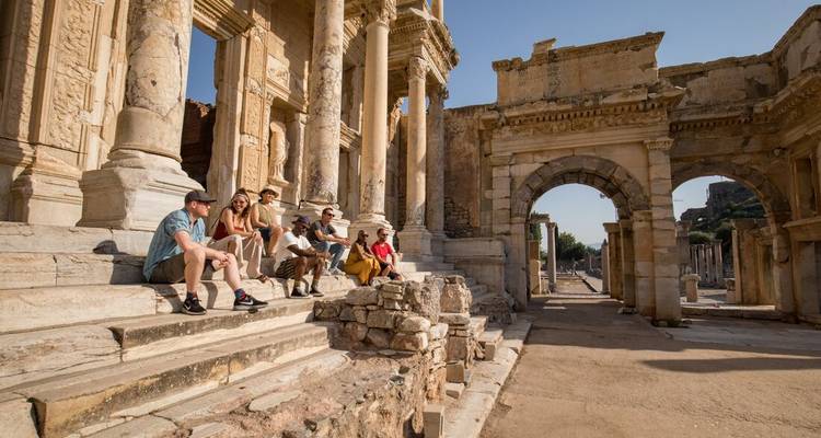 A group of people sitting on the steps of ancient ruins.