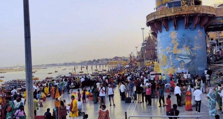 Drukke rivieroever met talrijke bezoekers en tempels op de achtergrond.