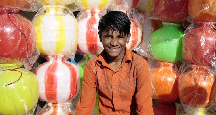 Glimlachende jongen zittend voor kleurrijke ballonnen.