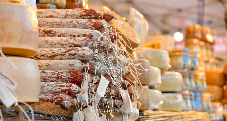 Des piles de saucisses séchées et des meules de fromage à un étal du marché italien.