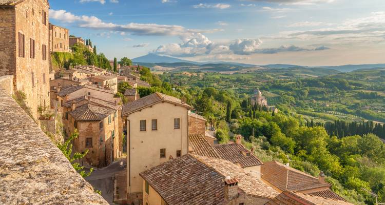 Vue panoramique des maisons en pierre s'étalant en cascade vers les vallées toscanes verdoyantes.