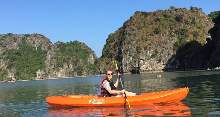 Personne faisant du kayak près de falaises rocheuses sous un ciel bleu dégagé.