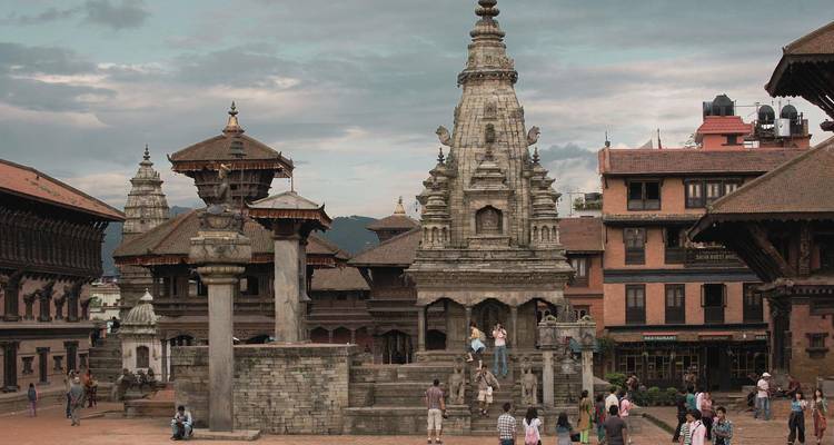 Menschen gehen auf einem historischen Platz mit verzierten Gebäuden und bewölktem Himmel spazieren.