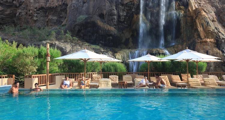 Des personnes se détendant dans une piscine avec une cascade en arrière-plan.
