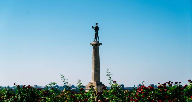 Estatua en una columna alta con flores en primer plano.