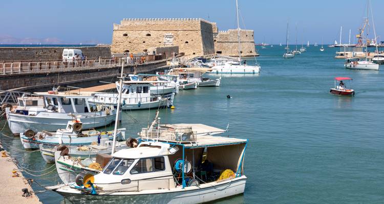 Fortaleza veneciana de piedra vigilando un puerto lleno de pequeños botes de pesca.