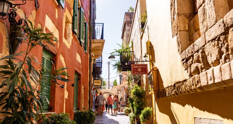 Callejón veneciano colorido con plantas en macetas, boutiques y turistas paseando.