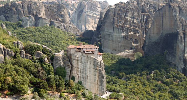 Monasterio de Meteora encaramado en lo alto de un pilar de roca imponente rodeado de acantilados espectaculares y bosque.