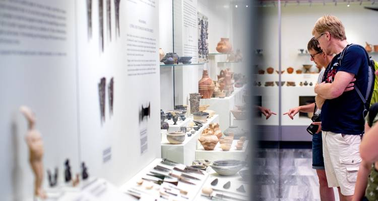 Les visiteurs du musée discutent des artefacts en céramique et des outils exposés dans des vitrines.