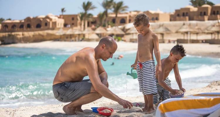 Man and two boys playing with sand on a beach.