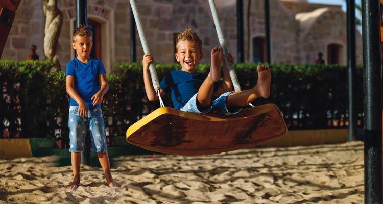 Two boys on a swing in a playground.