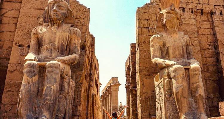 Persona entre dos estatuas de faraón de piedra sentadas.