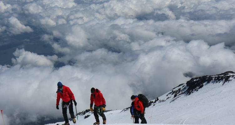 Des grimpeurs gravissant une montagne enneigée avec des nuages en contrebas.