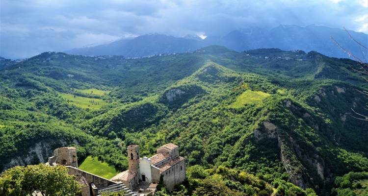 Lush green valleys with historical ruins, mountain range in the background.