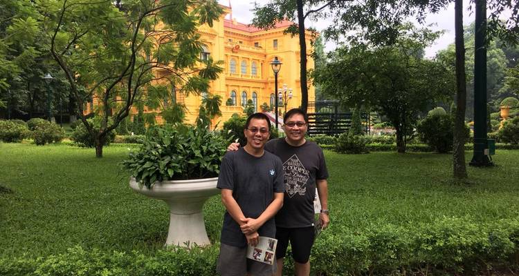 Zwei Personen stehen in einem Garten mit einem gelben Gebäude im Hintergrund.