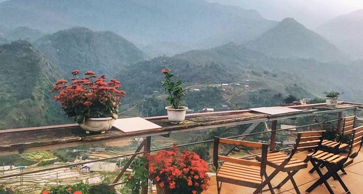 Mountain view with potted plants and chairs on a balcony.