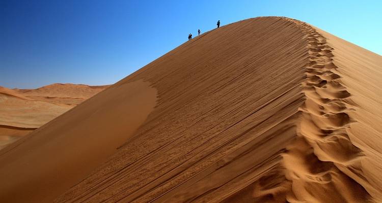 Une vaste dune de sable avec des empreintes de pas qui montent vers le sommet.