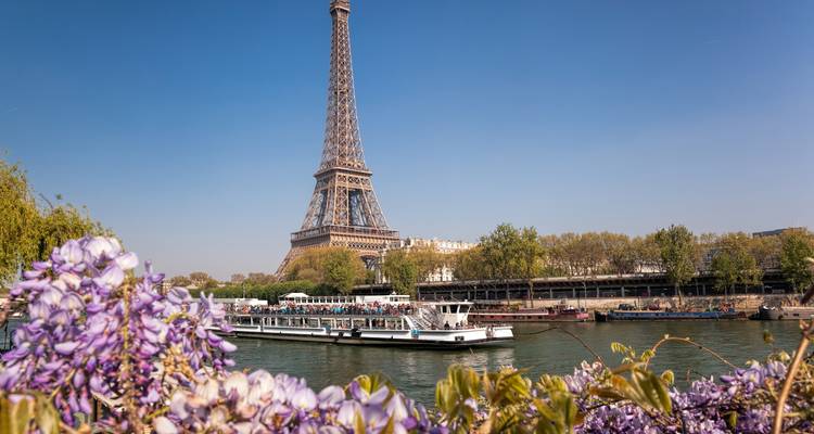 Vista de la Torre Eiffel con un crucero fluvial y flores en primer plano.