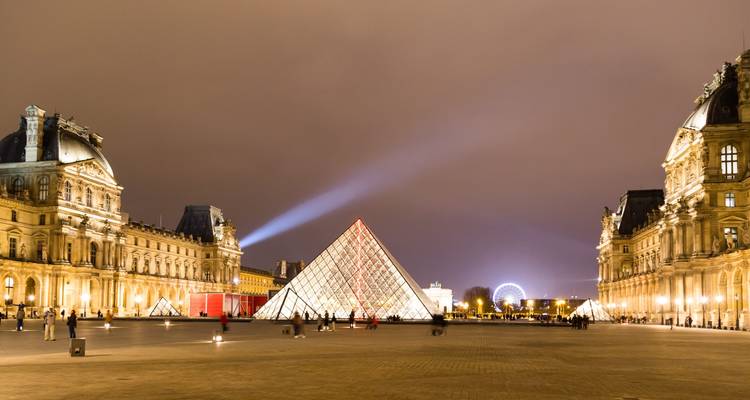 Vue nocturne de la Pyramide du Louvre avec des gens autour.