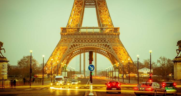 Vue de la Tour Eiffel illuminée la nuit avec la circulation environnante.