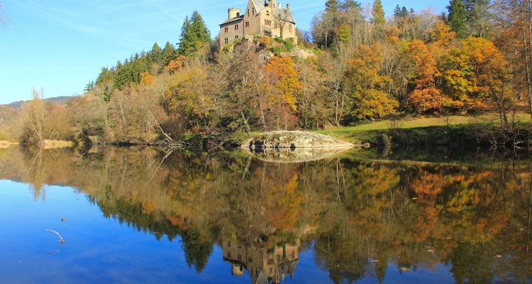 Château se reflétant dans une rivière calme avec un feuillage d'automne.