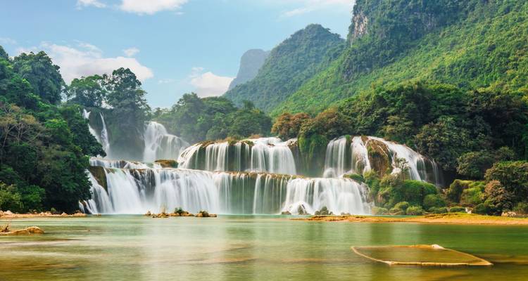 Ein majestätischer, mehrstufiger Wasserfall stürzt über üppig grüne Felsen in ein smaragdgrünes Becken.