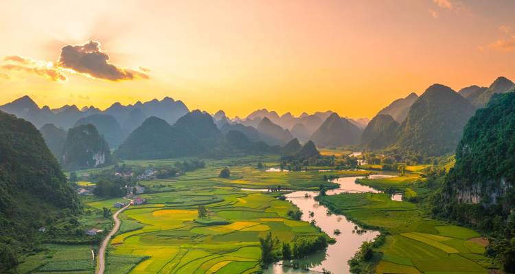 Vue aérienne au coucher de soleil sur des rizières en damier et une rivière sinueuse encadrées par des collines karstiques.