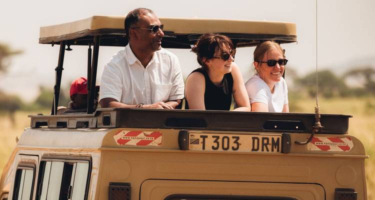 Des touristes se lèvent par la trappe de toit d'une jeep de safari en admirant les vues à travers la savane.