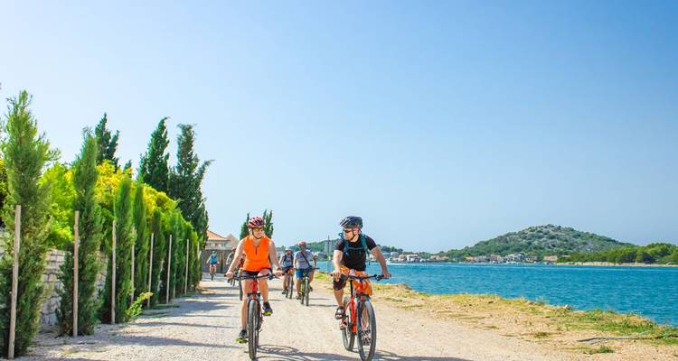 Cyclistes roulant le long d'un sentier côtier avec une eau bleue claire et de la verdure.