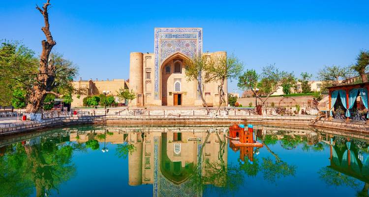 Una madraza histórica que se refleja perfectamente en un estanque tranquilo bajo un cielo azul brillante en Bujará.