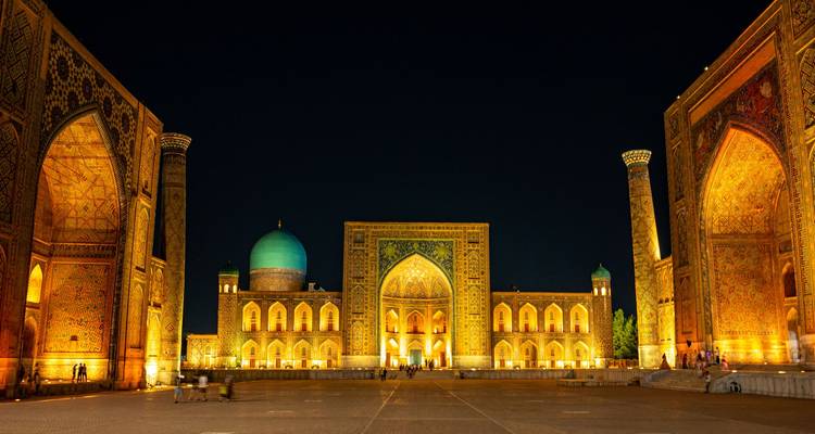 La Plaza Registan en Samarcanda iluminada por la noche, mostrando una magnífica arquitectura islámica y cúpulas doradas.