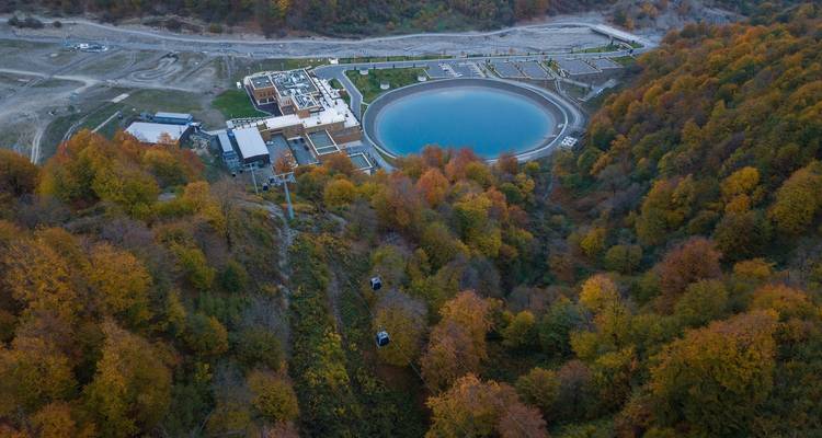 Vue aérienne d'un complexe hôtelier avec une piscine circulaire et une forêt environnante.